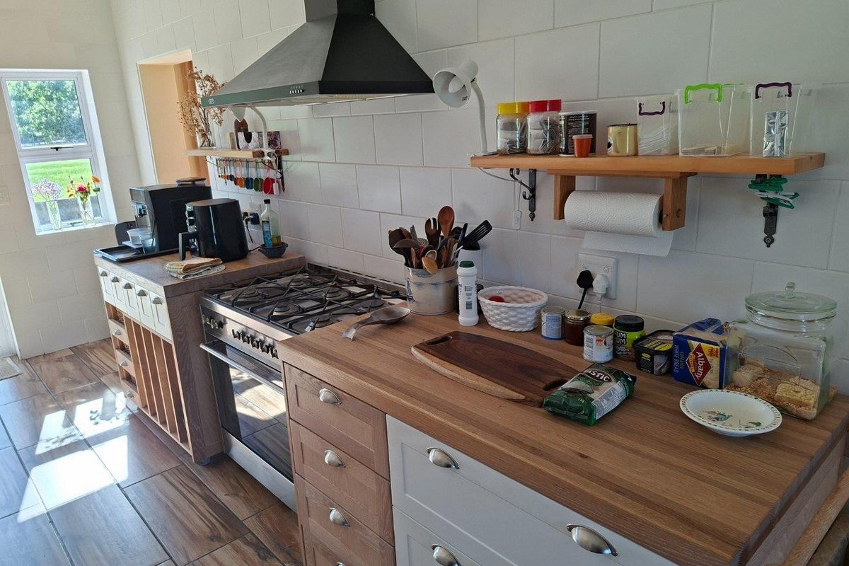 A functional kitchen featuring wooden countertops, white cabinetry, a gas stove with an extractor fan, and tiled flooring.
