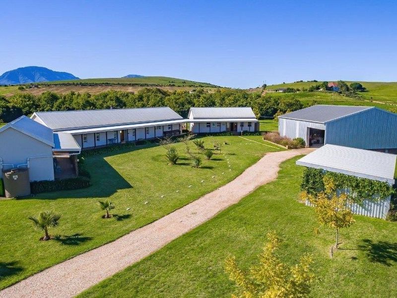 Aerial view of a farm property featuring multiple outbuildings, a large shed, and a gravel driveway set within a spacious rural landscape.