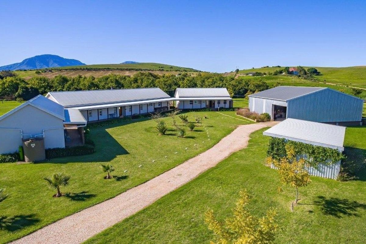 Aerial view of a farm property featuring multiple outbuildings, a large shed, and a gravel driveway set within a spacious rural landscape.