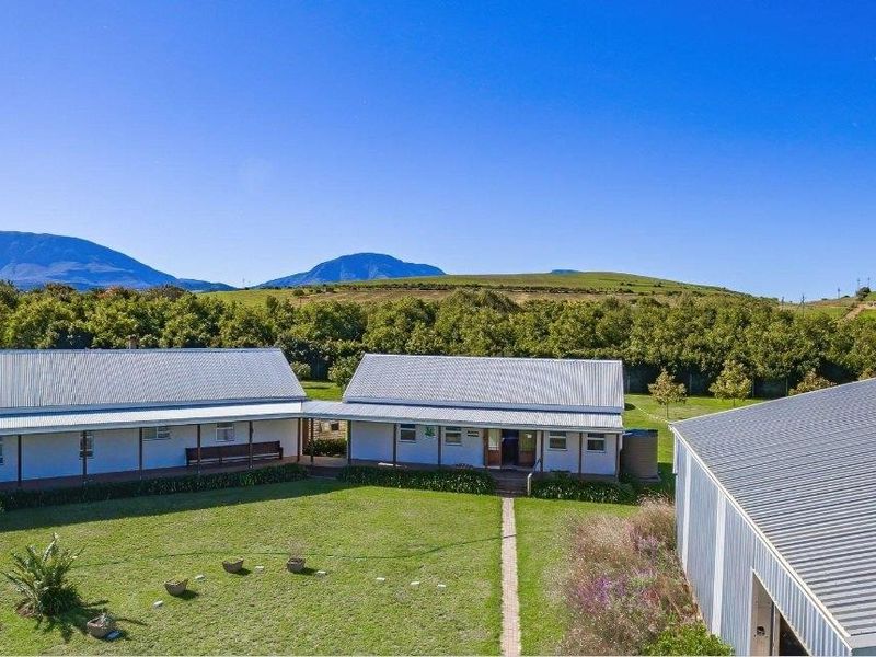 Aerial view of the farm property featuring multiple outbuildings with corrugated metal roofing, a central lawn, and expansive mountain landscape views.