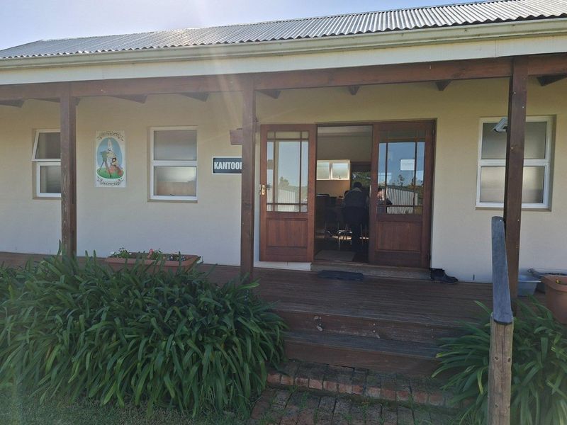 Exterior view of a farm office building featuring a covered timber veranda, wooden double doors, and corrugated metal roofing.
