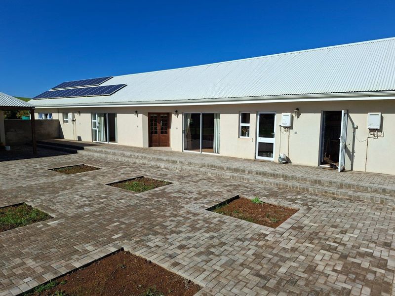 Rear view of the farm property featuring a paved courtyard, multiple access points, and roof-mounted solar panels.