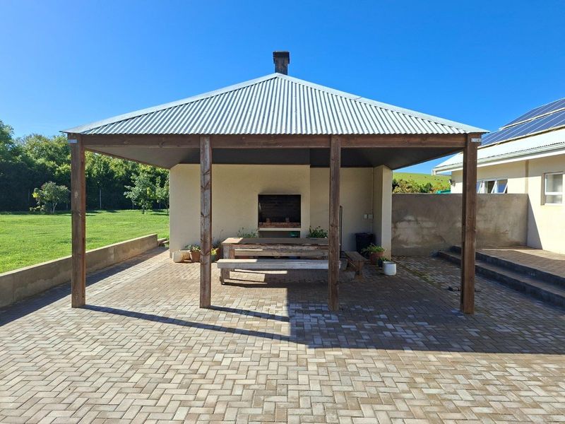 A covered outdoor patio area featuring a built-in brick braai, timber support beams, and paved flooring, ideal for outdoor entertaining.