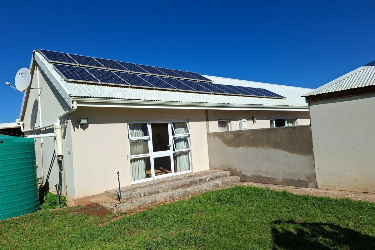 Rear exterior view of the farmhouse featuring a corrugated metal roof with installed solar panels, a water storage tank, and a paved patio area.