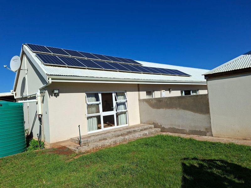 Rear exterior view of the farmhouse featuring a corrugated metal roof with installed solar panels, a water storage tank, and a paved patio area.