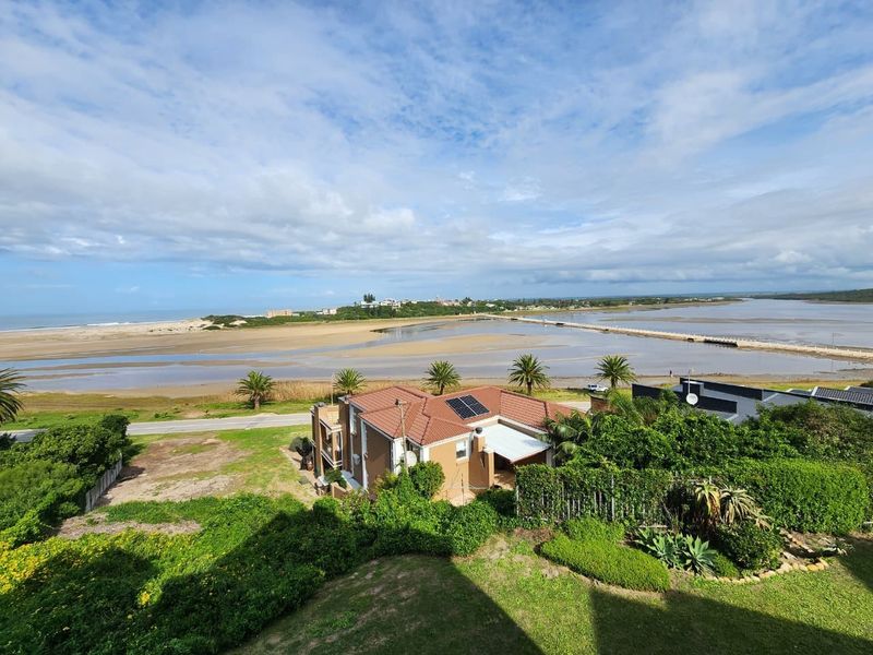 Elevated aerial view showcasing the property's coastal location, featuring a tiled roof, solar panels, and expansive views of the estuary and coastline.