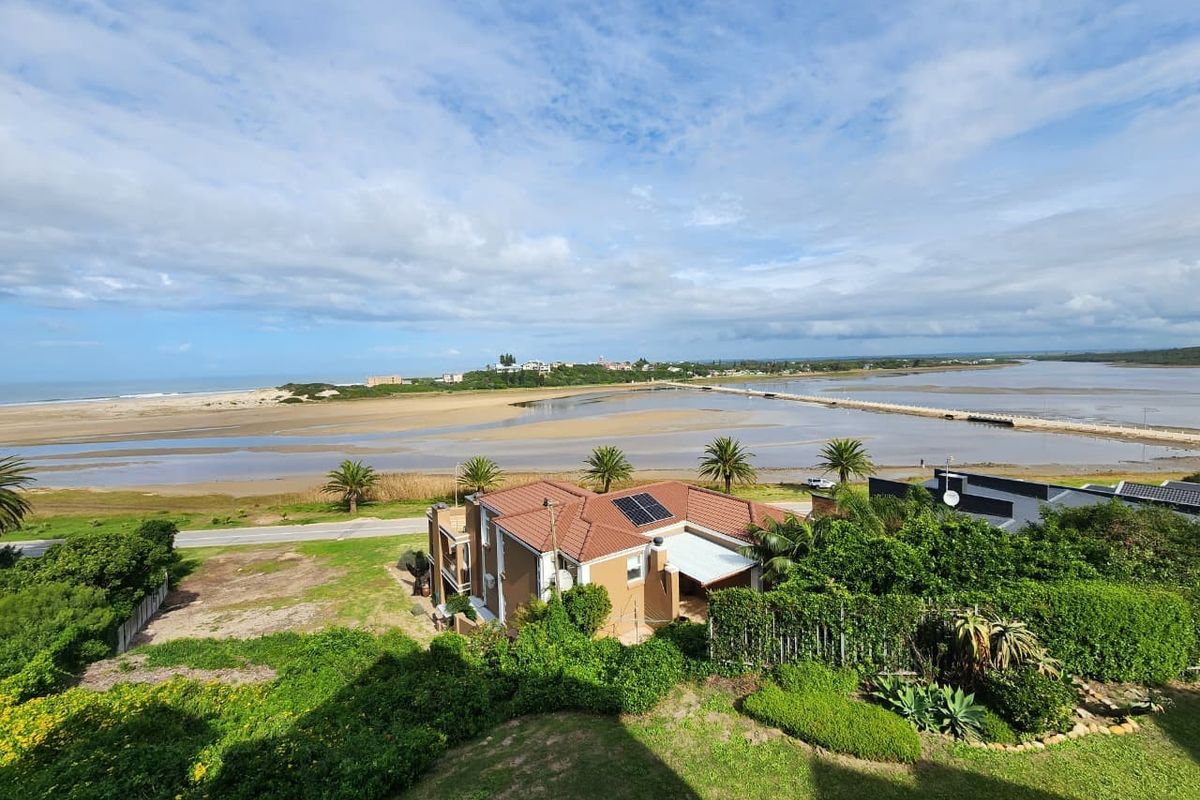 Elevated aerial view showcasing the property's coastal location, featuring a tiled roof, solar panels, and expansive views of the estuary and coastline.