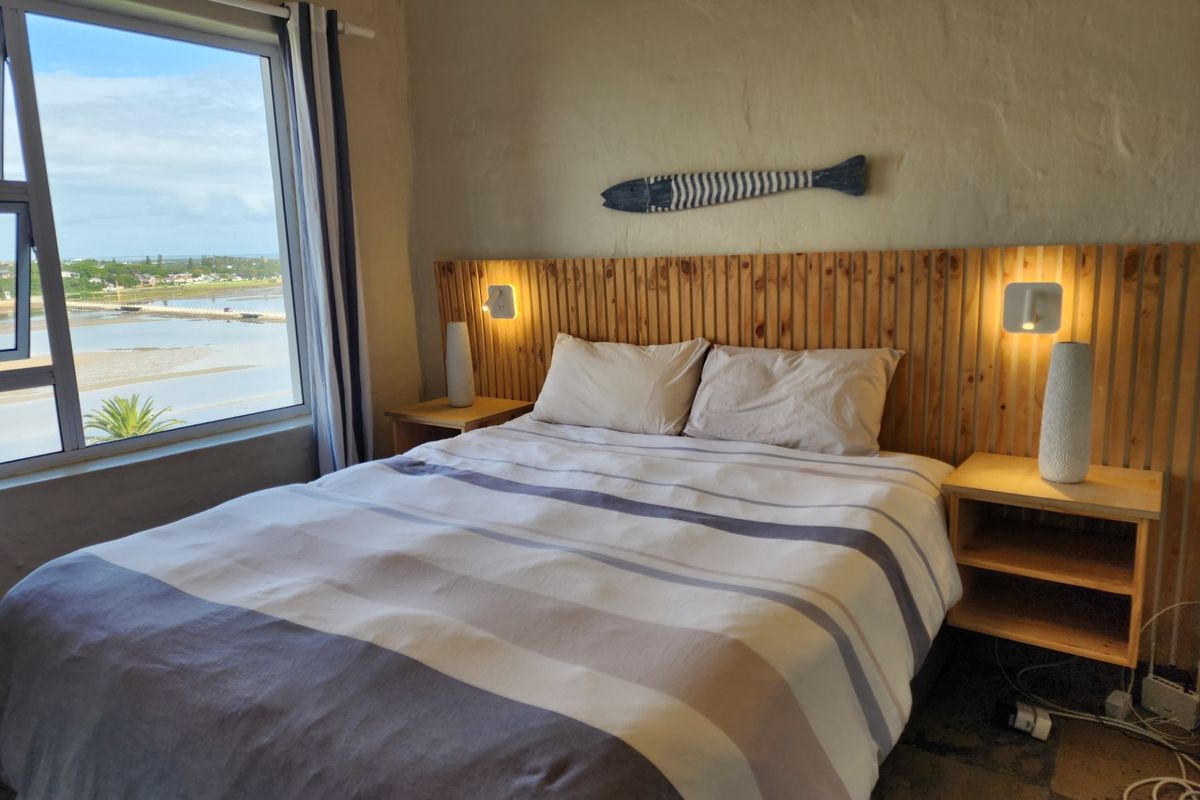 A bedroom featuring a custom timber slat headboard with integrated lighting and a large window offering scenic water views.