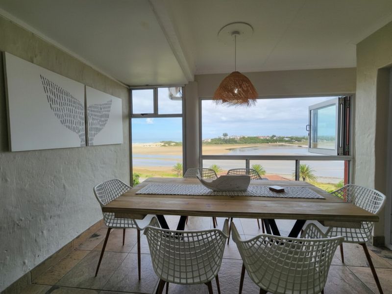 A bright dining area featuring large windows with scenic coastal views, tiled flooring, and a pendant light fixture.