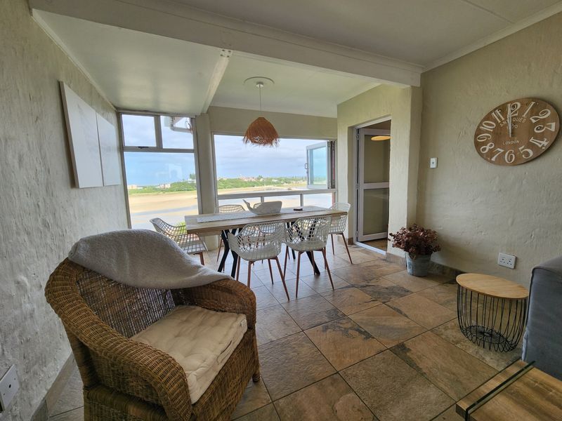A bright, open-plan living and dining area featuring large windows with scenic coastal views and durable tiled flooring.