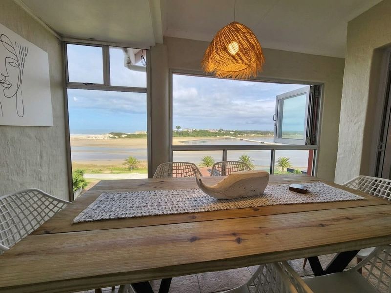 A bright dining area featuring large windows with expansive coastal and estuary views, tiled flooring, and a modern pendant light fixture.