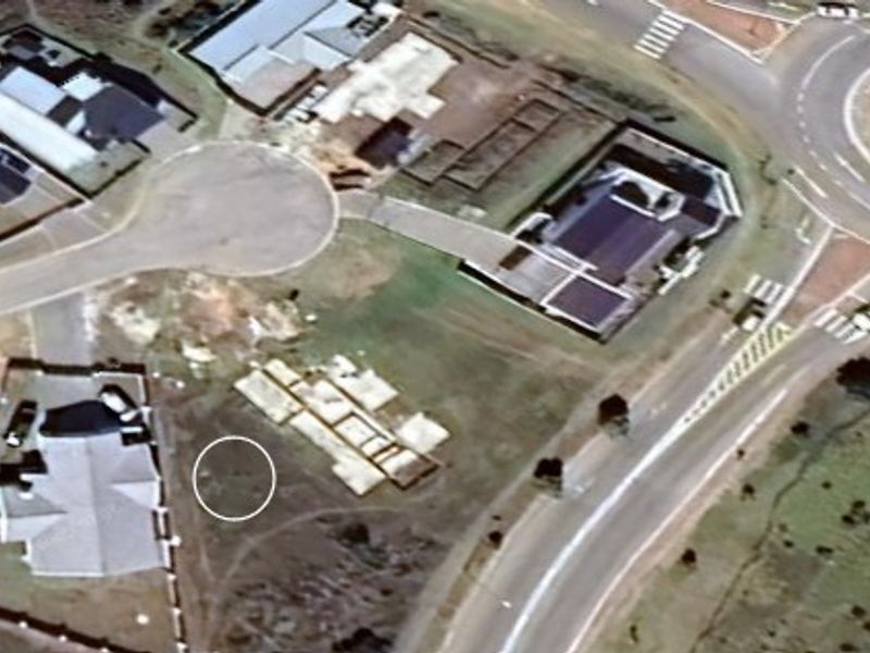 Aerial view of a vacant residential plot featuring a concrete foundation slab, situated within a developed suburban estate near a roundabout.