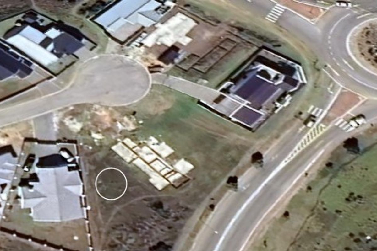 Aerial view of a vacant residential plot featuring a concrete foundation slab, situated within a developed suburban estate near a roundabout.