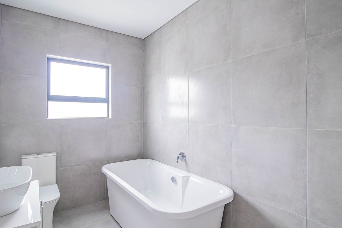 A modern, minimalist bathroom featuring large-format grey wall tiles, a sleek freestanding bathtub, and a contemporary vanity basin.