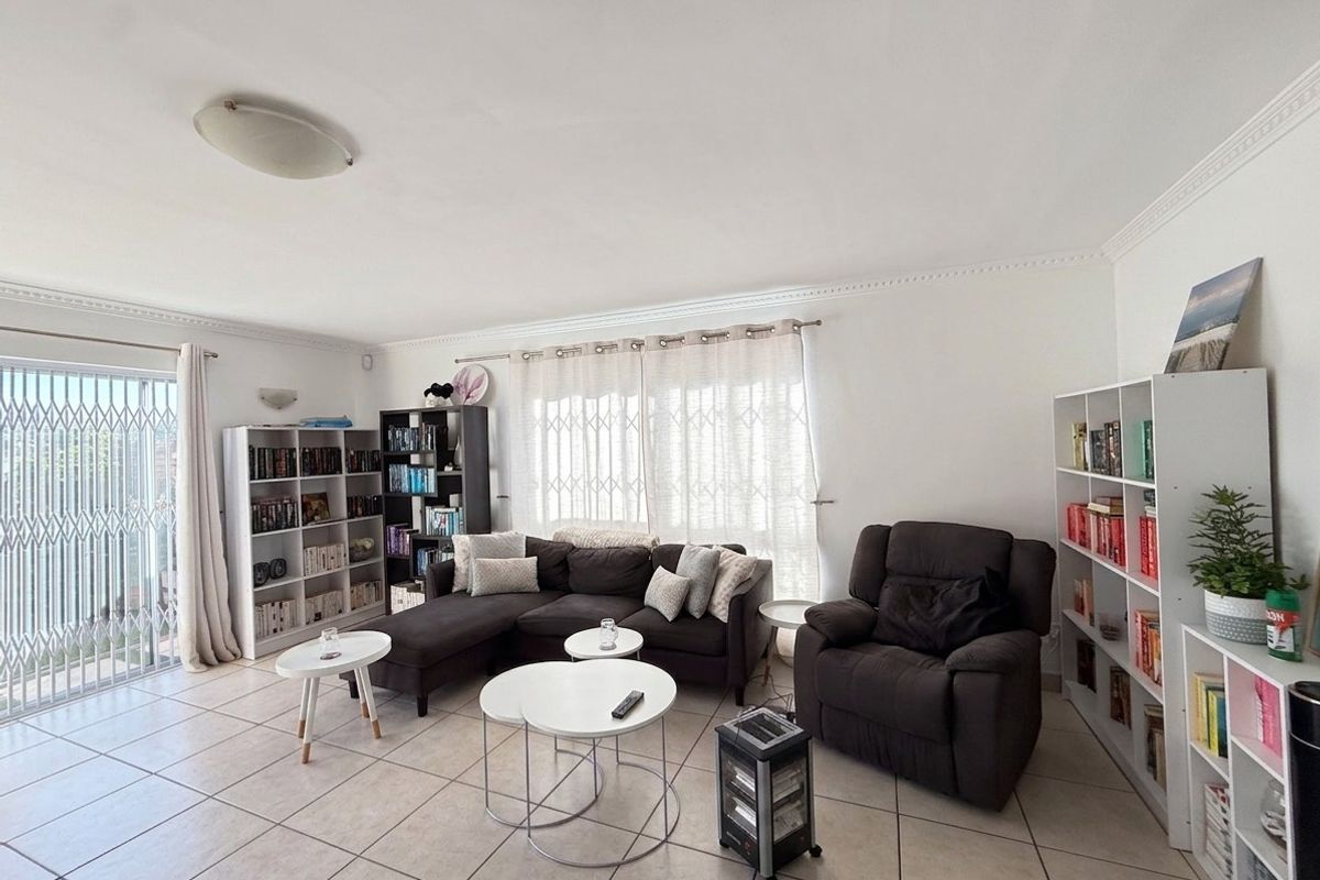 A spacious living room featuring neutral floor tiles, decorative crown molding, and sliding glass doors with security gates leading to an outdoor area.