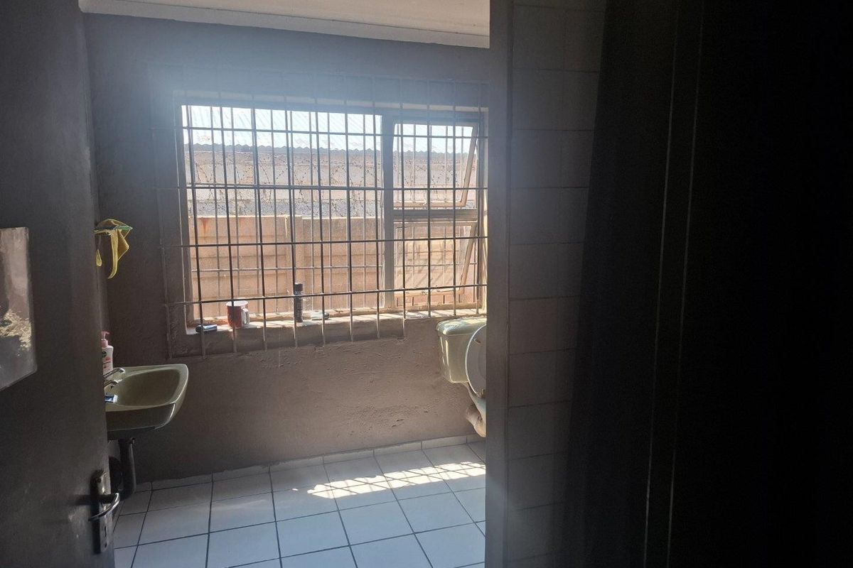 A functional bathroom featuring tiled flooring, a wall-mounted basin, and a toilet, with security bars installed on the window.