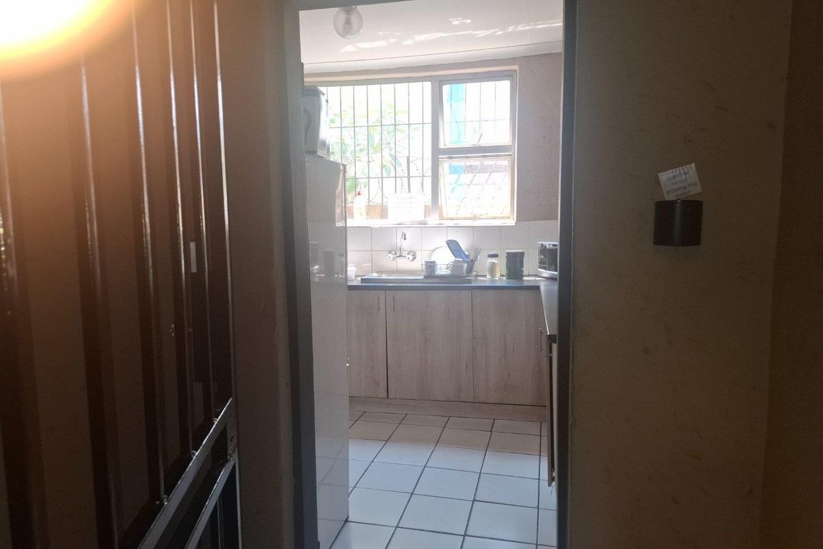 A functional kitchen area featuring tiled flooring, built-in cabinetry, and a sink, viewed through a doorway with security gate.