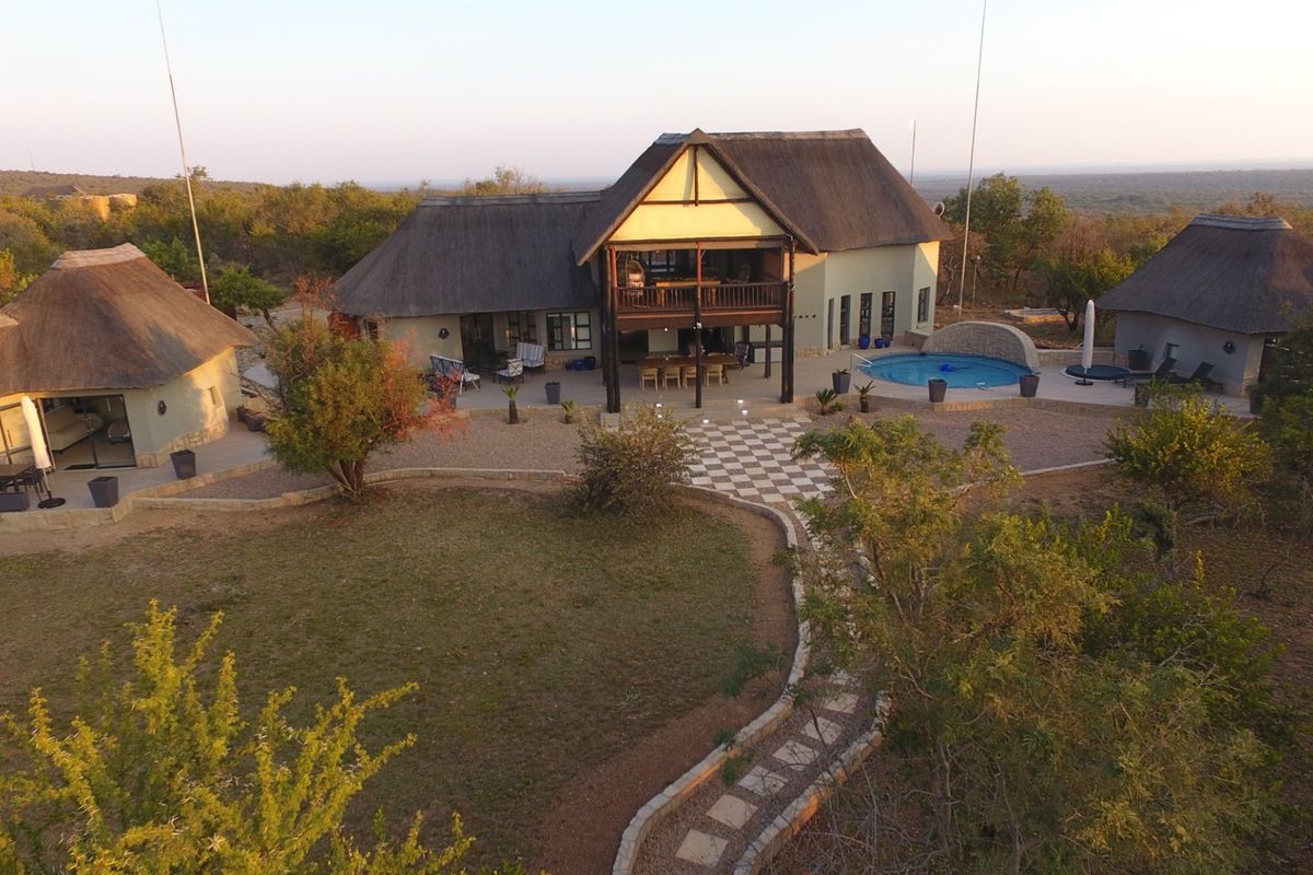 Aerial view of a spacious property featuring multiple thatched-roof buildings, a central swimming pool, and landscaped garden areas in a natural bushveld setting.