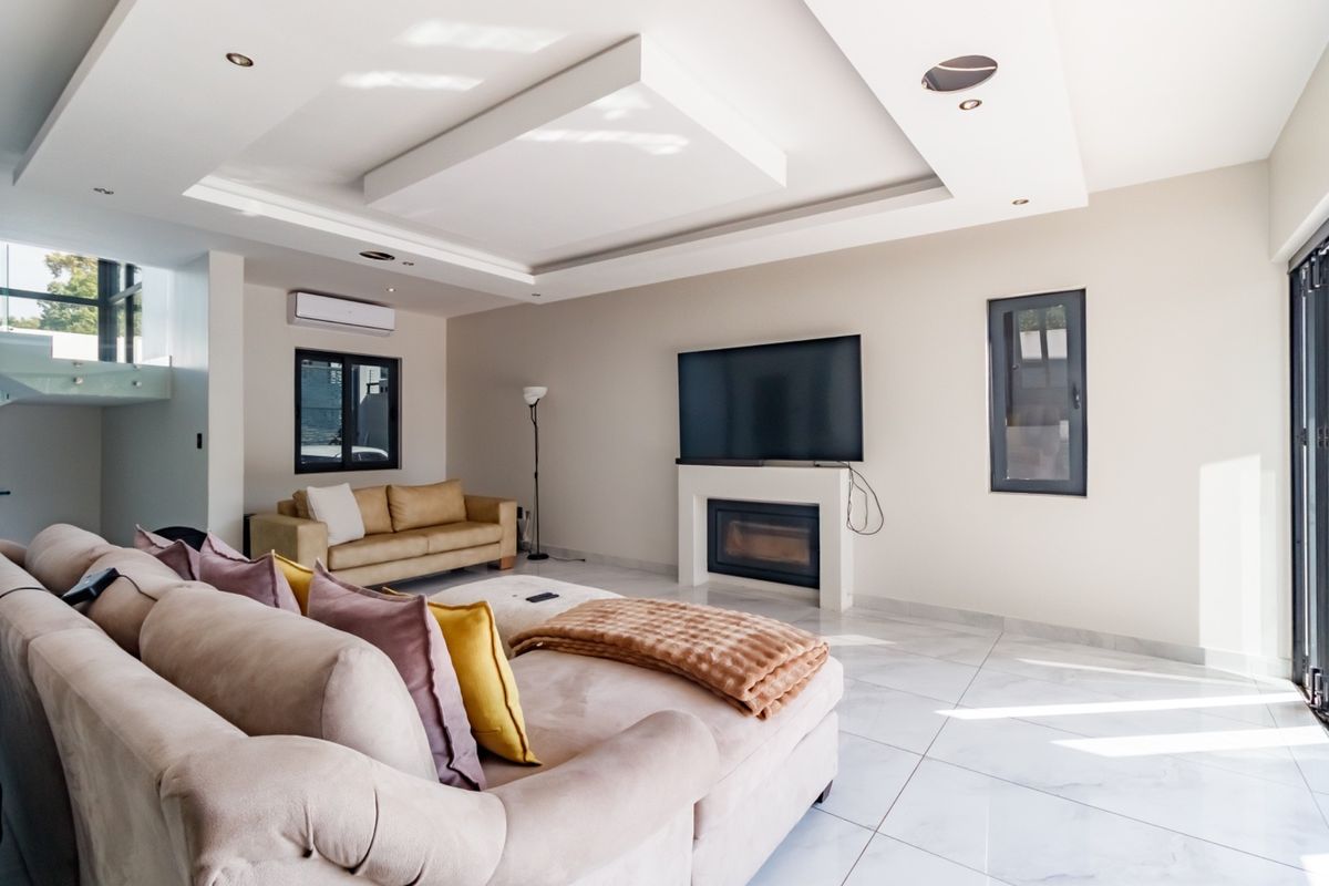 Modern living room featuring a built-in fireplace, recessed tray ceiling with downlights, tiled flooring, and split-system air conditioning unit.