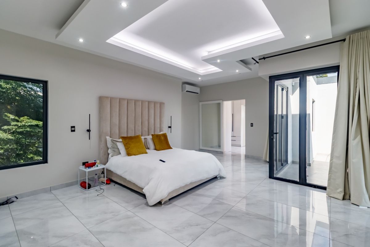 Spacious modern bedroom featuring a coffered ceiling with recessed lighting, marble-look tiled flooring, air conditioning unit, and direct access to an outdoor patio area.
