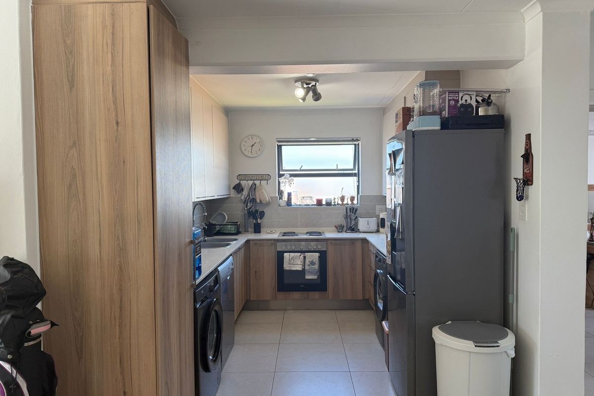 A functional U-shaped kitchen featuring wood-look cabinetry, tiled flooring, a built-in oven, and a hob, providing efficient workspace and storage.