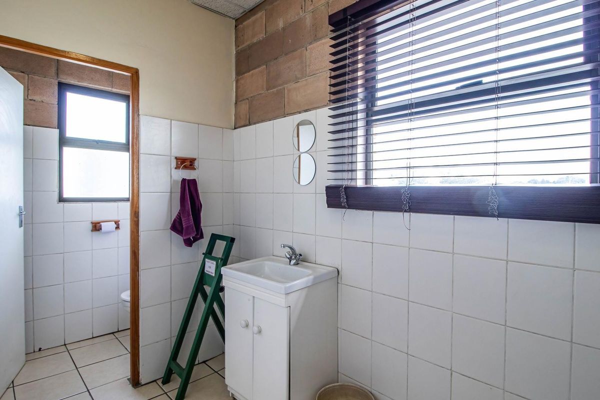 A functional bathroom featuring a vanity basin, tiled walls, and exposed concrete block detailing, requiring cosmetic updates to improve its overall condition.