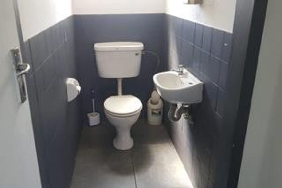 A compact commercial restroom featuring a standard toilet, wall-mounted basin, and dark tiled wall accents.