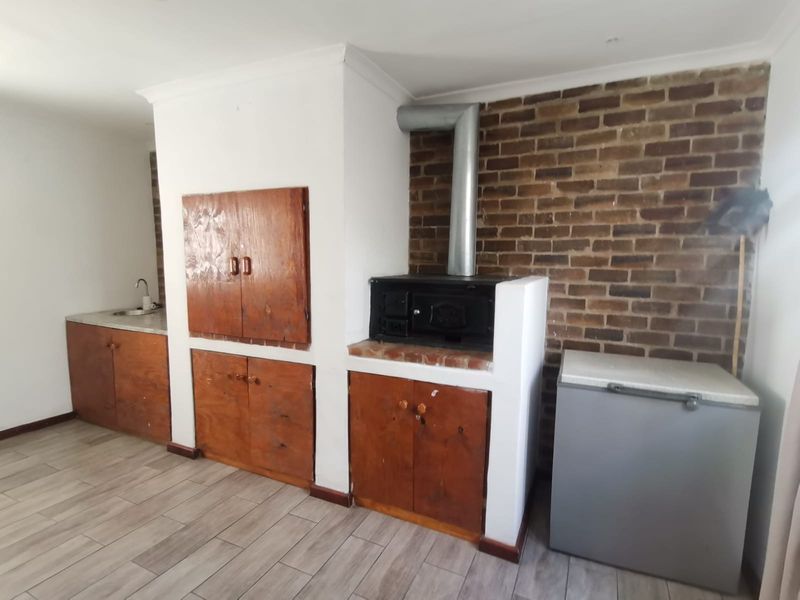 A functional kitchen area featuring built-in wooden cabinetry, a brick feature wall, and a built-in wood-burning stove with a metal flue.