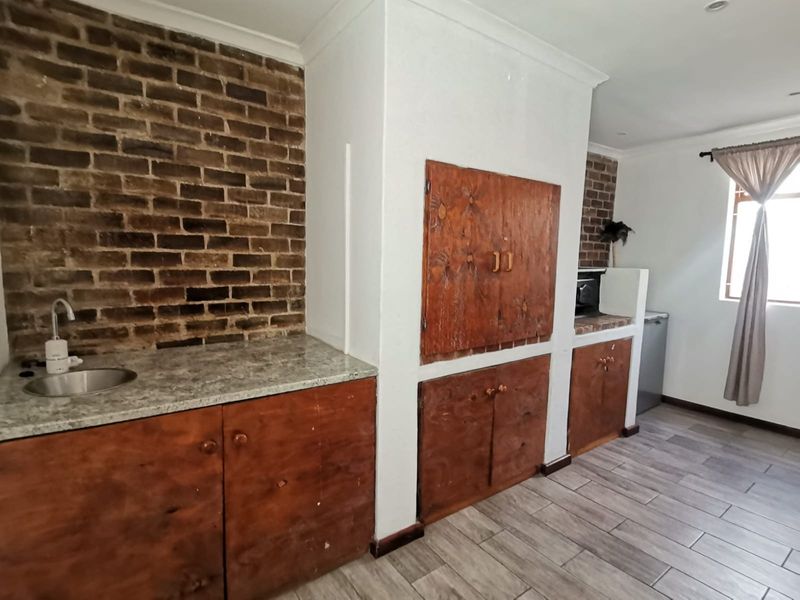 A functional kitchen area featuring exposed brick accents, stone-look countertops, and built-in wooden cabinetry with tiled flooring.