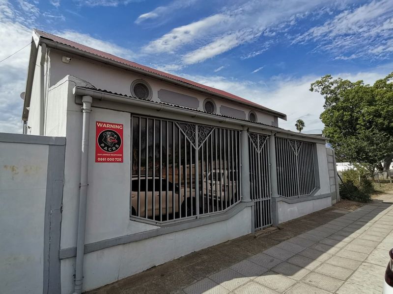 Front exterior view of the property featuring a secure boundary wall with integrated metal security bars and a corrugated metal roof.
