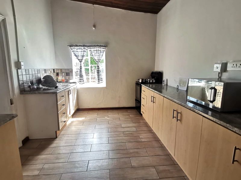 A functional kitchen featuring light wood cabinetry, granite-look countertops, tiled flooring, and a vaulted timber ceiling.
