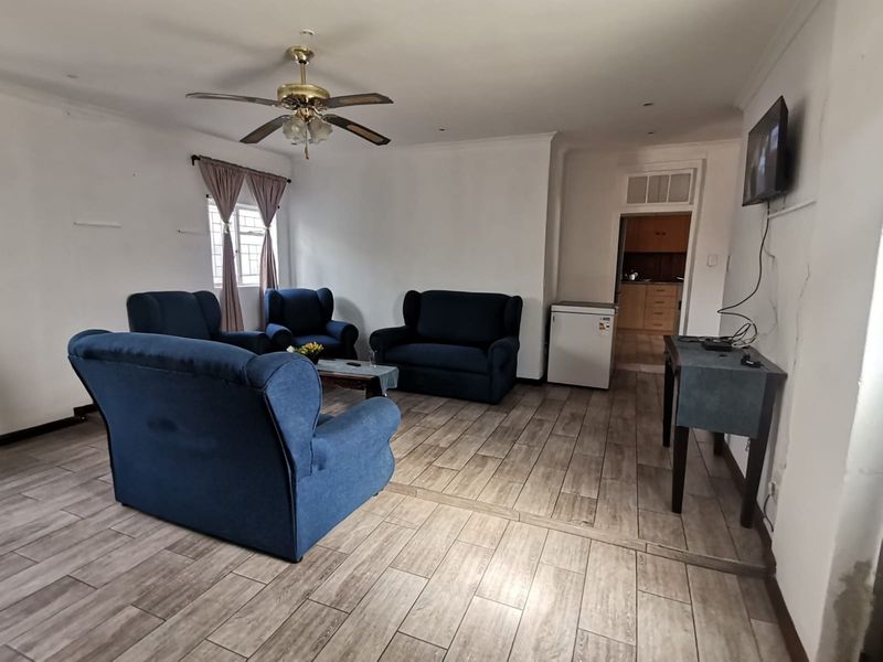 Spacious living area featuring wood-look tiled flooring, a ceiling fan, and an open-plan layout leading to a kitchen area.