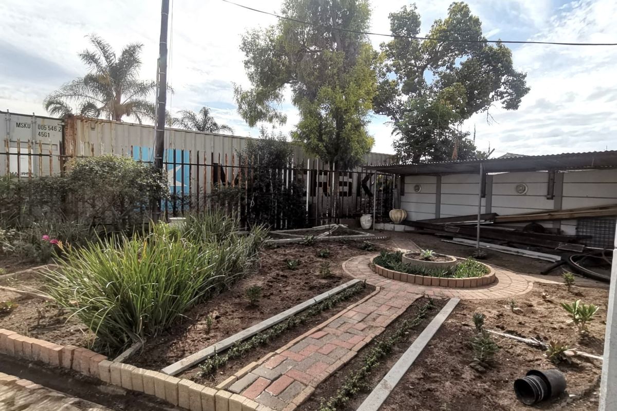 A rear garden area featuring brick pathways, a circular planter, and perimeter fencing, currently requiring landscaping and maintenance to improve its overall appeal.