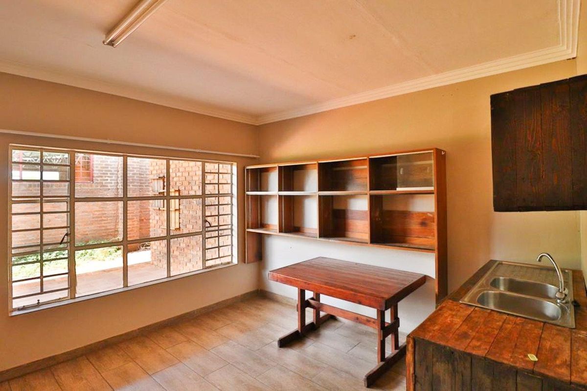 A functional kitchen area featuring a double stainless steel sink, wooden cabinetry, and large windows providing natural light and views of the exterior.