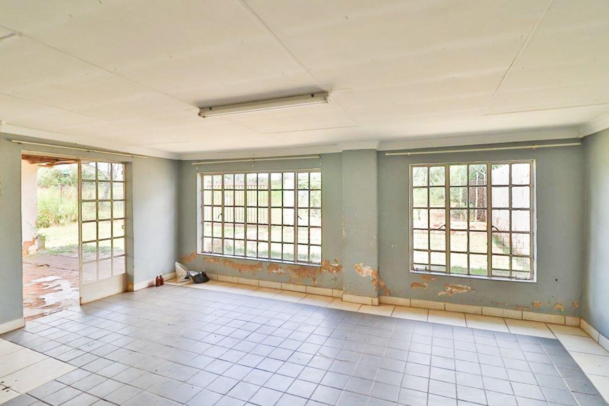 An empty, sunlit living area featuring tiled flooring, large grid-style windows, and direct access to an outdoor patio space.