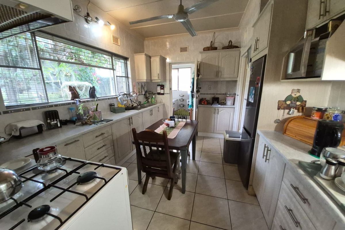 A functional kitchen featuring light-toned cabinetry, tiled countertops, a gas stove, and a ceiling fan, with an adjacent dining area and tiled flooring.