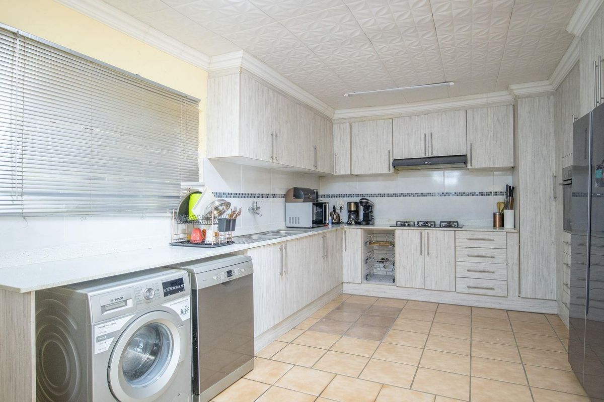 A functional kitchen featuring light wood-grain cabinetry, tiled flooring, a built-in gas hob with extractor fan, and integrated space for laundry appliances.