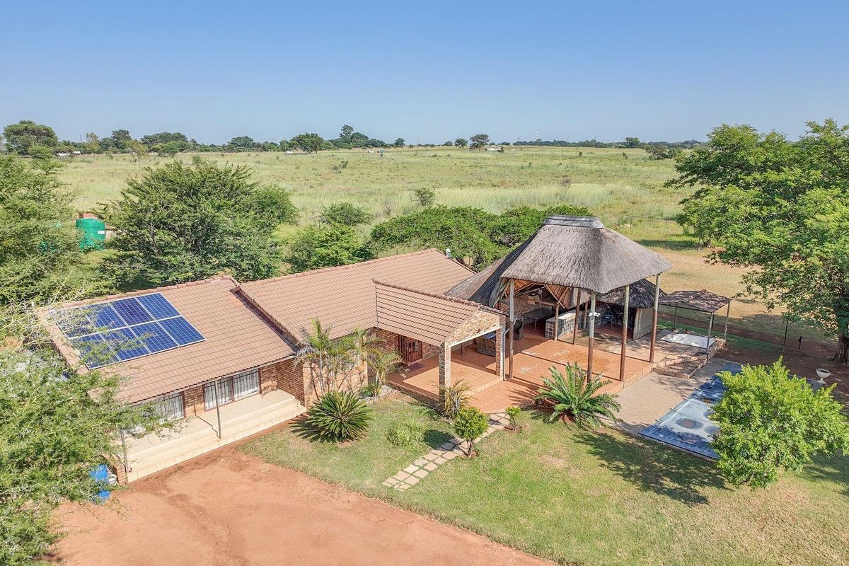 Aerial view of a farm property featuring a tiled roof residence with solar panels, a thatched lapa entertainment area, and a swimming pool.