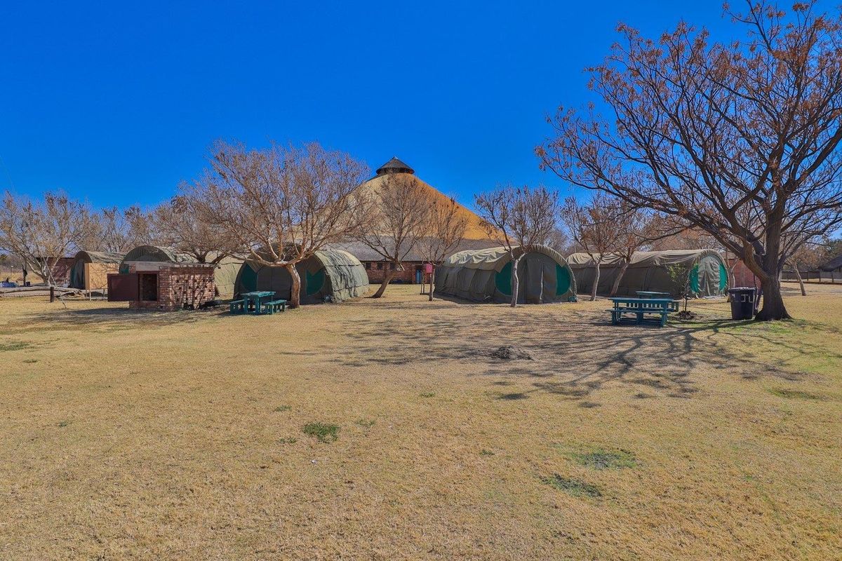 Expansive farm grounds featuring a large thatched-roof main structure and several semi-permanent tented accommodation units set within a spacious, open landscape.