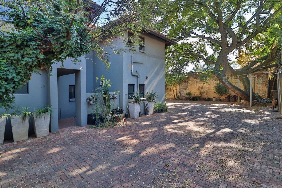 Rear exterior view of the commercial property featuring a brick-paved courtyard, mature trees, and a weathered boundary wall.