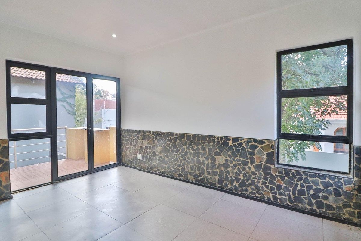 An empty living area featuring stone wall cladding, large aluminium windows, and a sliding door leading to an outdoor balcony.