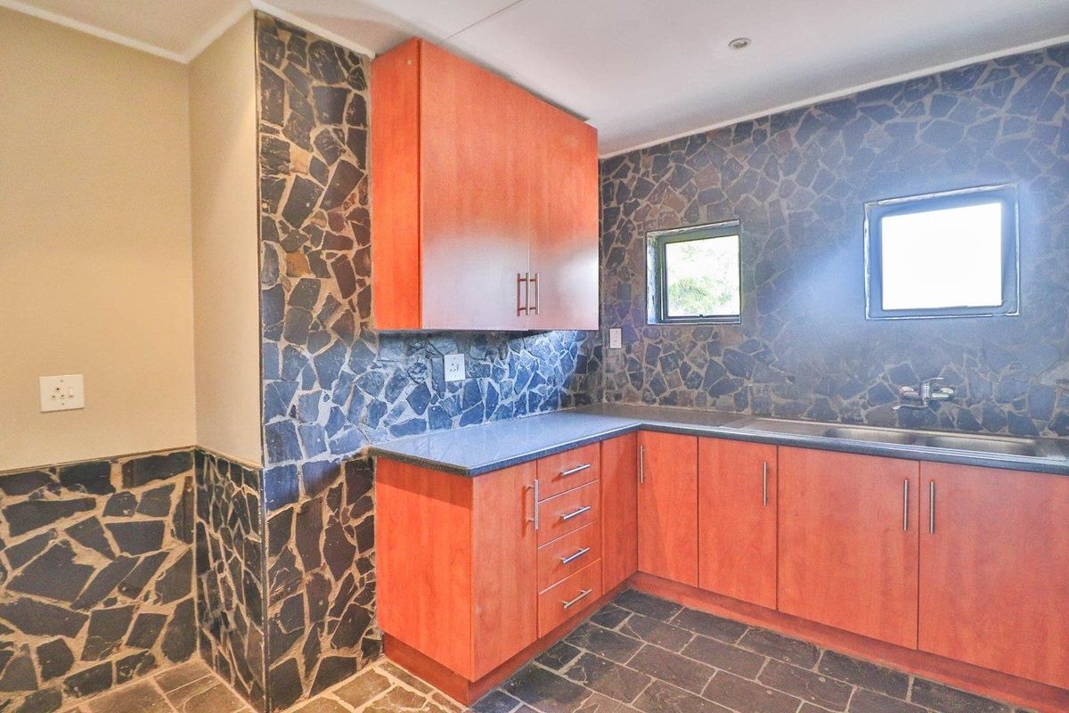 A functional kitchen featuring wood-look cabinetry, stone countertops, a stainless steel sink, and distinctive stone wall cladding throughout the space.