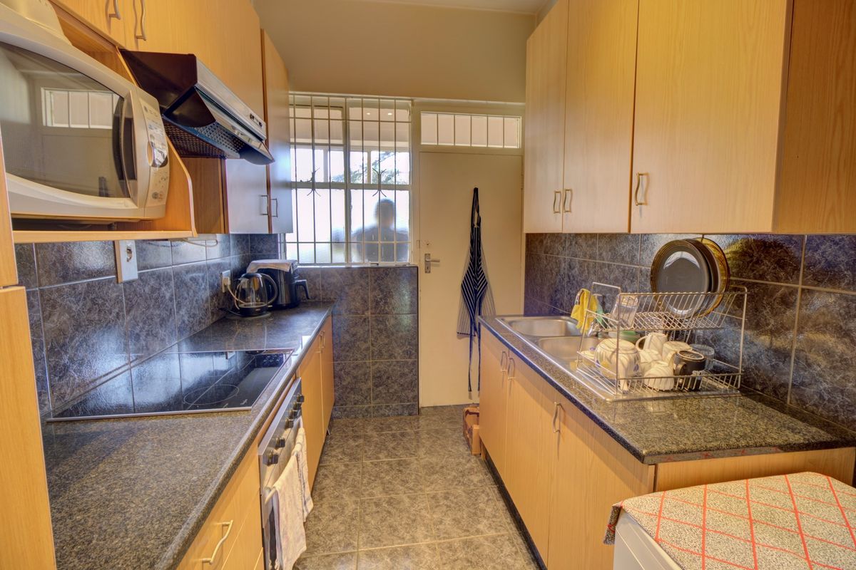 A functional galley-style kitchen featuring light wood cabinetry, dark granite countertops, a built-in hob, oven, and extractor fan with tiled splashbacks.