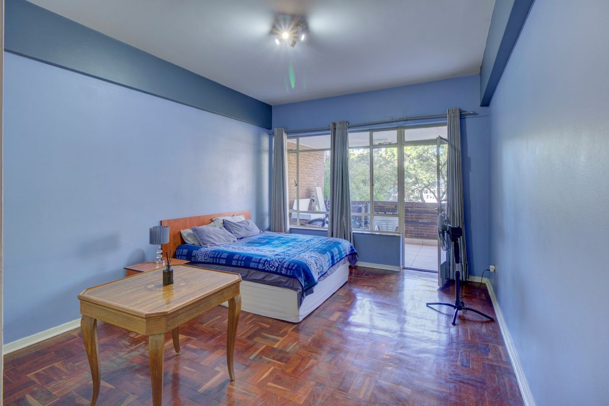 Spacious bedroom featuring original parquet flooring, large windows, and direct access to a private balcony.