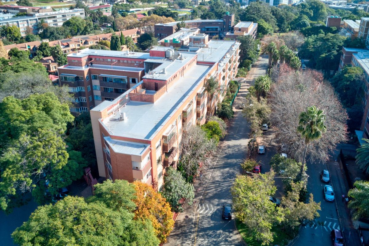Aerial view of a multi-story brick apartment complex situated in a leafy, established residential neighborhood with mature trees and surrounding street infrastructure.
