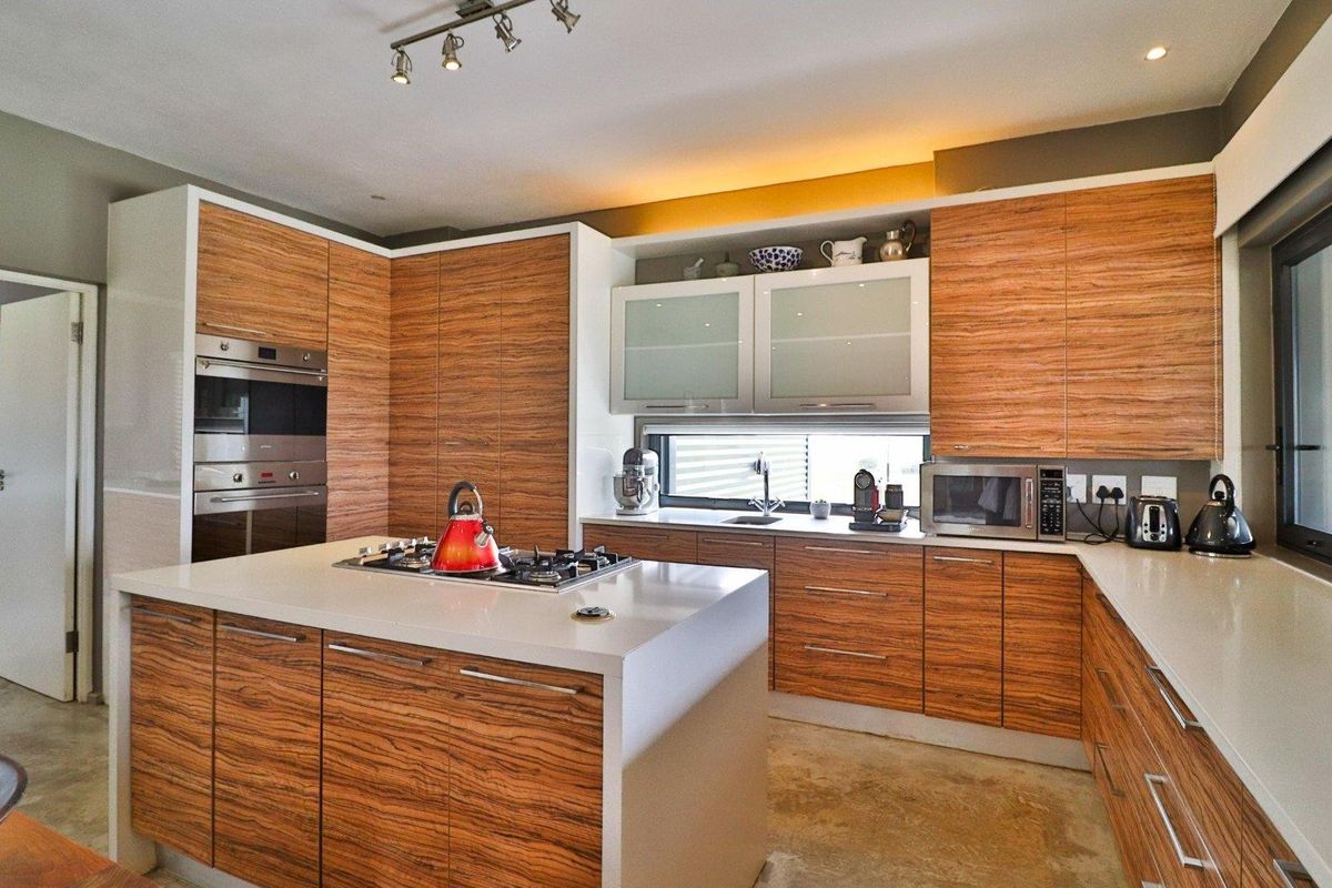 Modern kitchen featuring wood-grain cabinetry, stone countertops, a central island with a built-in gas hob, and integrated stainless steel oven and microwave.