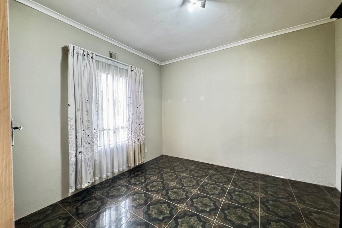 A vacant bedroom featuring patterned ceramic floor tiles, neutral wall paint, and a window with fitted curtain tracks.