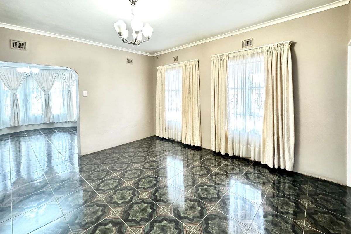 A spacious, empty living area featuring patterned ceramic floor tiles, arched entryway, and large windows with classic drapery.