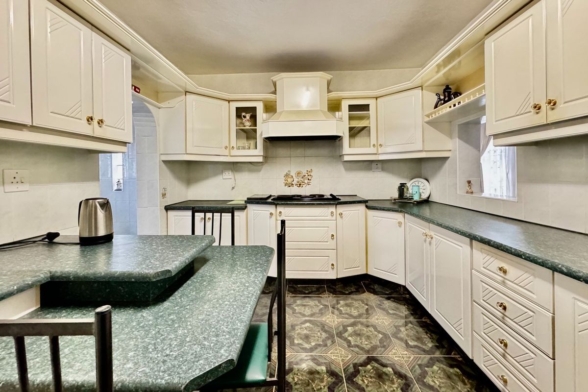 A functional kitchen featuring white cabinetry, a built-in hob with extractor fan, and a green laminate countertop with an integrated breakfast bar.