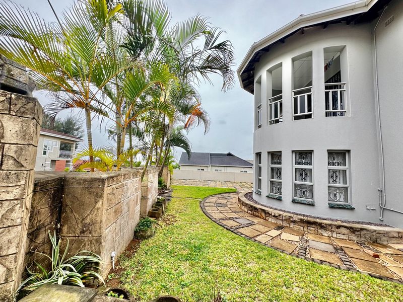 A view of the rear garden featuring a curved building facade, stone paved pathway, and established palm trees along the boundary wall.